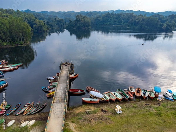 Fototapeta Mohamaya Lake is the second-largest artificial lake in Bangladesh, located in Mirsarai, Chittagong, Bangladesh. Aerial view of a tranquil lake with a pier and docked boats surrounded by lush greenery.