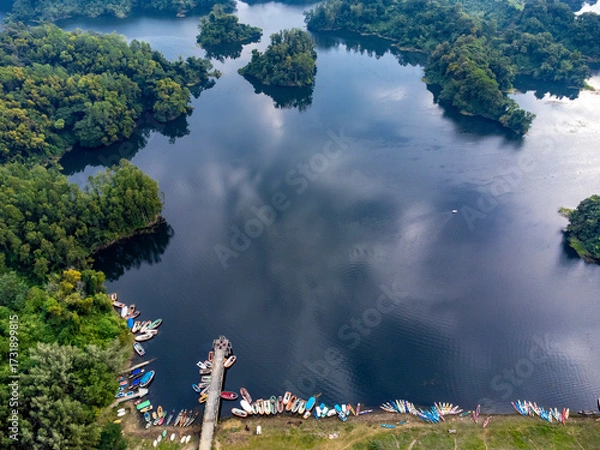 Fototapeta Mohamaya Lake is the second-largest artificial lake in Bangladesh, located in Mirsarai, Chittagong, Bangladesh. Aerial view of a tranquil lake with a pier and docked boats surrounded by lush greenery.
