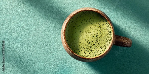 Fototapeta Ceramic cup filled with alexandrite green matcha latte on textured surface with copy space