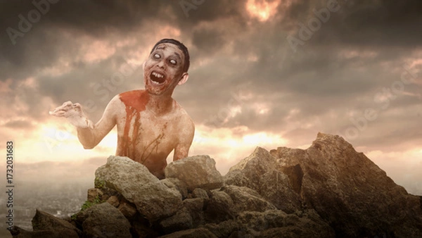 Fototapeta Scary male zombie with a wound and bloody crawling on rocky terrain. The scene is scary and creepy. Dramatic sky. Concept of Spooky Halloween