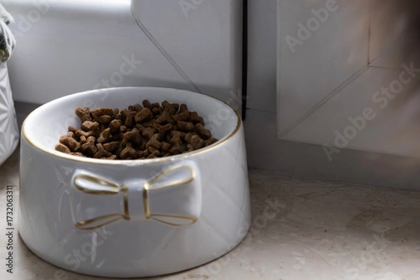 Fototapeta Pet food bowl designed with a bow holds kibble near a sunny window on a calm morning