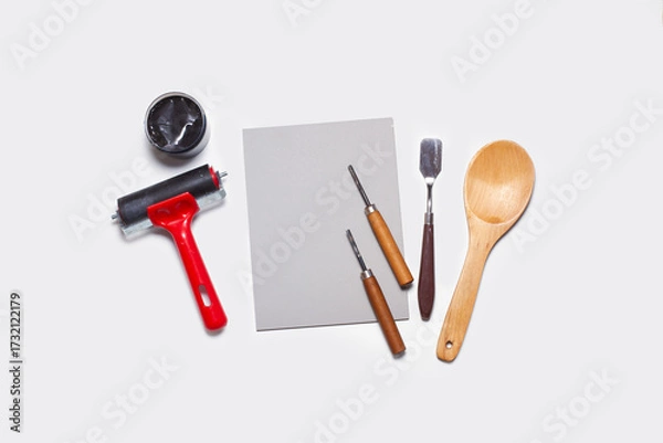 Fototapeta A sheet of linoleum, black ink, a screen printing roller, spatula, gouge and a wooden spoon on a white background