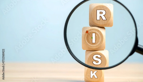 Obraz Magnifying glass focusing on wooden blocks with word RISK, symbolizing risk management and evaluation.