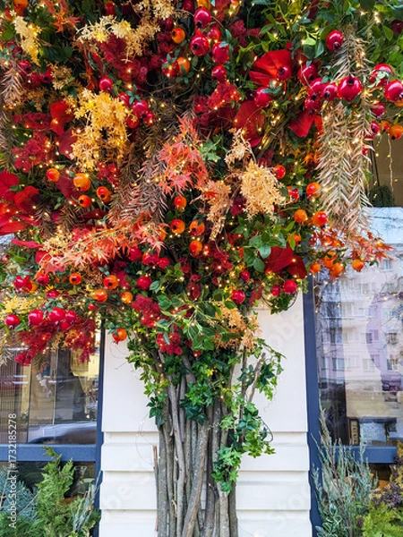 Fototapeta Exterior holiday decoration featuring a vibrant tree with red berries, golden leaves, glowing string lights, autumn foliage, and cozy seasonal atmosphere