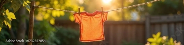 Fototapeta A single, colorful garment hangs gently swaying on a personal clothesline strung between two rustic posts in a sun-drenched backyard, creating a peaceful, domestic scene , line, colorful