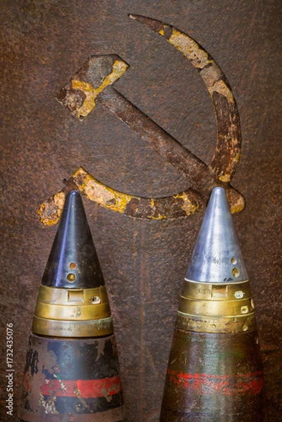 Fototapeta Two old military bombs in front of a weathered USSR hammer and sickle