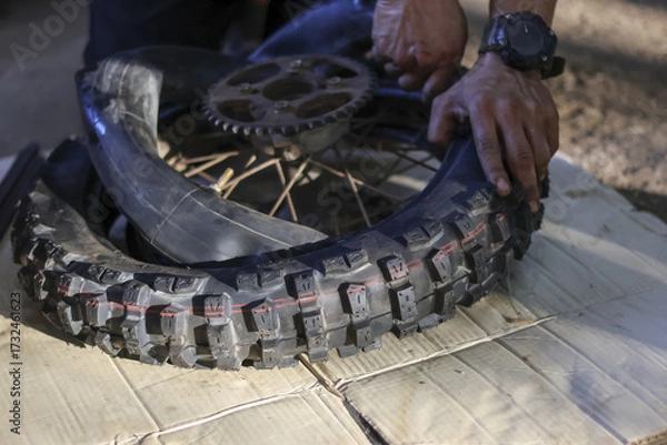 Fototapeta Focused individual diligently repairs flat motorcycle tire, carefully removing damaged inner tube for quick replacement. close up view captures hands process of vehicle maintenance, showcasing
