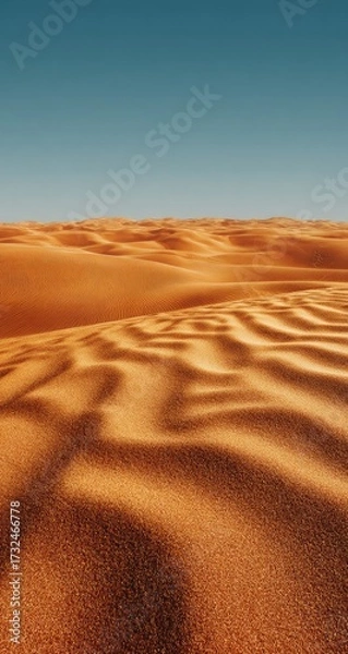 Fototapeta Undulating orange sand dunes stretch to a clear, deep blue sky, the texture of the sand emphasized by subtle shadows and light