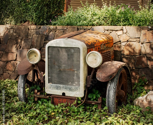 Fototapeta front end of a rusty old car against a stone wall