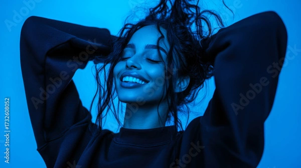 Fototapeta Smiling woman with curly hair enjoying blue ambient light in a cozy indoor setting at night