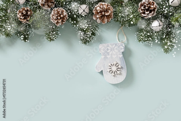 Fototapeta Christmas frame with evergreen branches and mitten of wooden natural materials, snowflakes on blue background. Copy space. Xmas vertical greeting card. View from above.