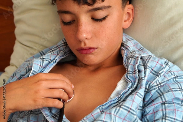 Fototapeta sick child in pajamas in bed, with stethoscope and look of discomfort