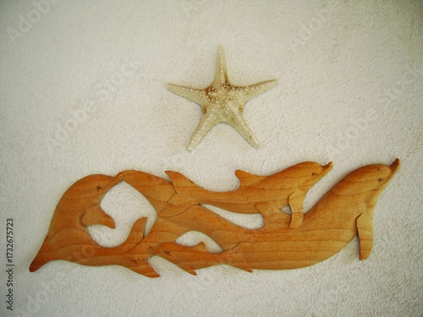 Obraz Wooden wall decoration featuring a pod of dolphins swimming together with a starfish above, mounted on a textured white surface, evoking a coastal and ocean theme.