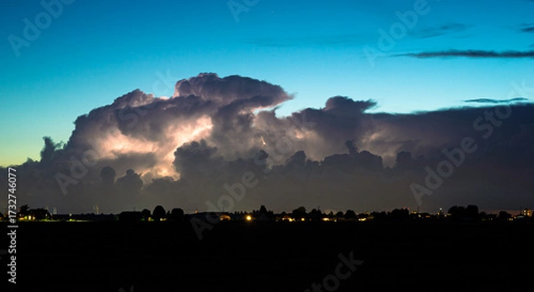 Fototapeta Distant storm clouds are illuminated by sheet lightning at dusk
