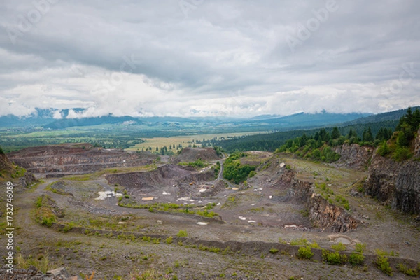 Fototapeta Quarry landscape with terraced rock formations, sparse vegetation and hills in the distance under a cloudy sky. Near Suseni in eastern Carpathians, Romania.