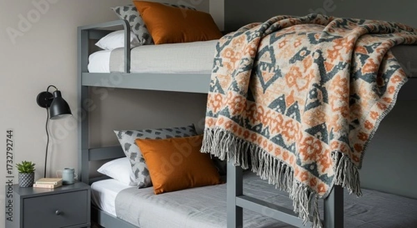 Fototapeta A grey bunk bed setup featuring cozy bedding, patterned throw pillows, and a vibrant patterned blanket draped over the top bunk.
