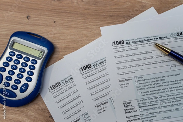 Fototapeta US tax forms 1040 for 2024, calculator, and pen on a wooden desk.