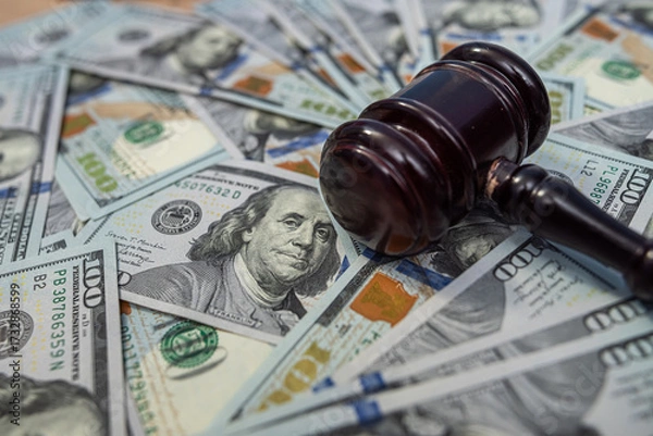 Fototapeta Wooden gavel on a background of US dollar banknotes, representing financial judgment.