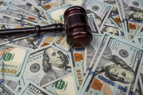 Fototapeta Wooden gavel on a background of US dollar banknotes, representing financial judgment.