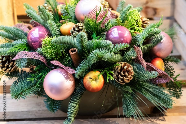 Fototapeta Christmas arrangement of fir and pine branches with pine cones, pink Christmas tree balls, apples and cinnamon sticks, selective focus