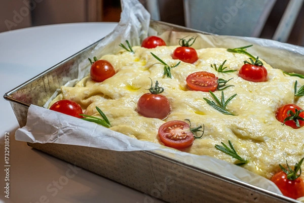 Fototapeta Focaccia dough topped with fresh cherry tomatoes and rosemary, resting in a baking pan, showcasing a deliciously fluffy texture and traditional preparation method