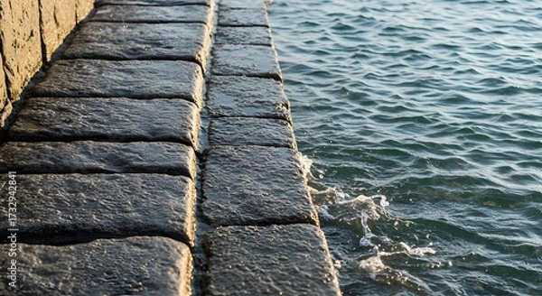 Fototapeta Stone steps meet the ocean waves creating a textured scene with water and stone elements visible close up