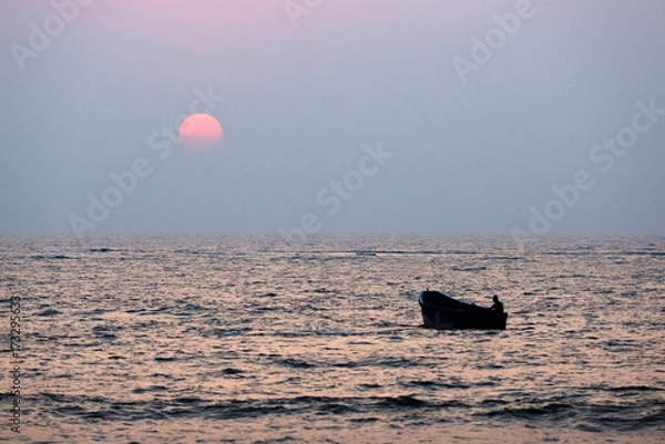 Fototapeta Fisherman sailing in a boat at sunset