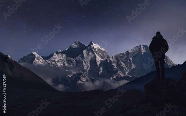 Fototapeta A man contemplating the mountains under the moonlight in a starry night