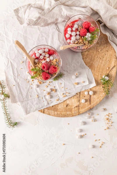Obraz An overhead shot of two glasses of layered raspberry and chia seed pudding with fresh raspberries and white crowberry on a rustic wooden platter
