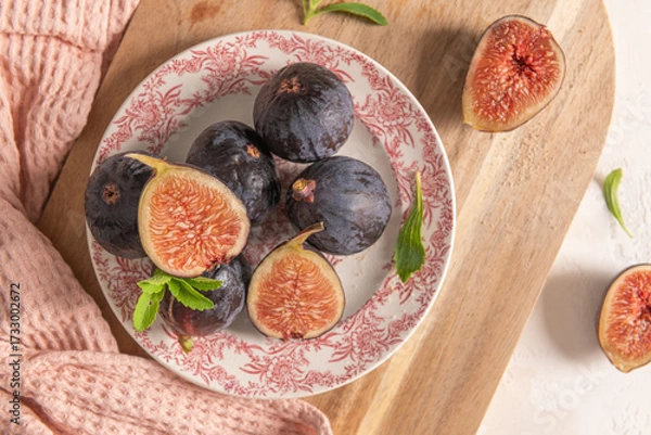 Obraz A rustic top-down view of a plate of fresh figs, a wooden board, fresh stevia leaves, and a pink napkin in soft light
