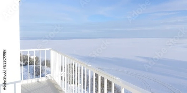 Fototapeta Wide frozen lake covered in snow under a pale blue sky seen from a white balcony