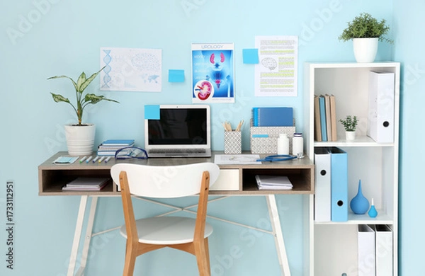 Fototapeta Medical student's workplace with blank laptop and study materials near blue wall in clinic