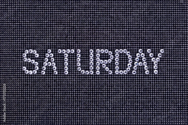 Fototapeta Day of the week, word SATURDAY is made rhinestones crystal color on a black canvas background.