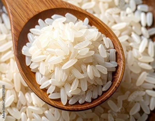 Fototapeta Close-up of raw white rice in a wooden spoon and on a table, top view