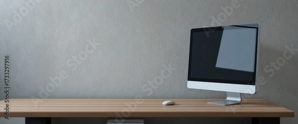 Fototapeta Modern desktop computer monitor and white mouse on a wooden desk against a textured gray wall
