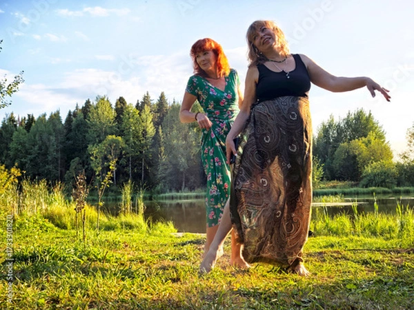 Fototapeta Two women enjoying a sunny day by the water in a lush green setting during summer