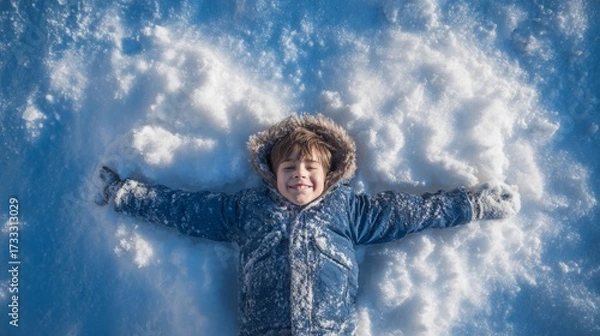 Fototapeta Child boy making a snow angel while smiling in winter snow  