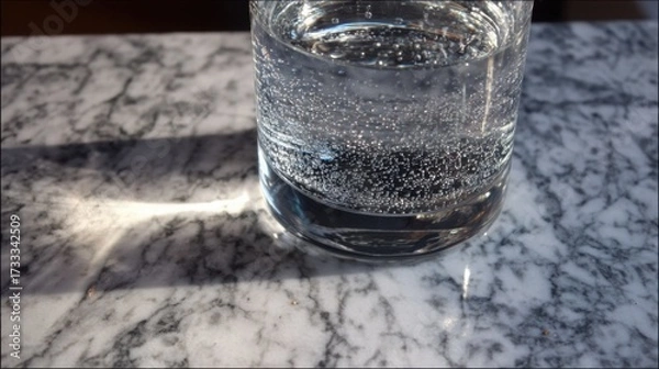 Obraz condensation. A close-up of a clear water glass with condensation on a sleek marble surface, reflecting light in a minimalist setting. bar promotions.