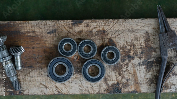 Obraz Close-up of metal ball bearings and machine gears on a wooden workbench. Mechanical parts and industrial tools for repair, engineering, and maintenance concepts.