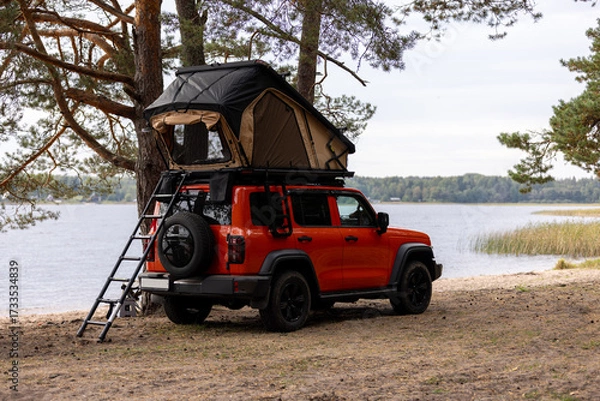 Obraz A car with a tent on the roof on the sandy shore of the lake