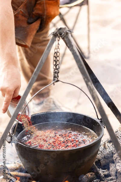 Fototapeta Cooking at the campsite, adding a spice mixture to the cauldron