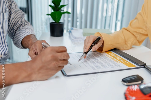 Fototapeta A businesswoman in a yellow suit is consulting with a male client about car purchase contracts, showing documents and car models on the desk to finalize agreement and transaction.