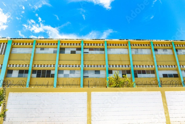 Obraz Pedernales, Dominican Republic, 8 august 2025. View of the facade of a typical Dominican school, paintend bright yellow against a blue sky.