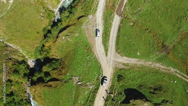 Obraz A top-down aerial view of two cars of travelers driving along a dirt road one after the other.