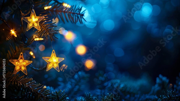 Fototapeta Christmas lights. Golden stars string hanging at fir branches in navy defocused background. Holiday card. Copy space for text.