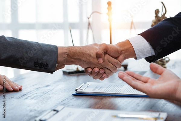 Fototapeta Lawyers or business partners shaking hands after reaching an agreement or closing a deal, with a contract on the table