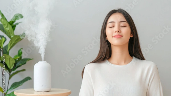 Fototapeta Woman enjoying calm and relaxation with essential oil diffuser in serene indoor setting. soft mist creates tranquil atmosphere