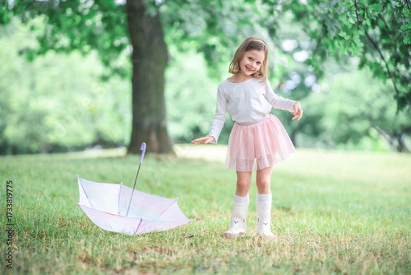 Fototapeta Little girl spinning with arms wide near an umbrella on the ground. A dreamy and natural moment of freedom and imaginative play in the rain.