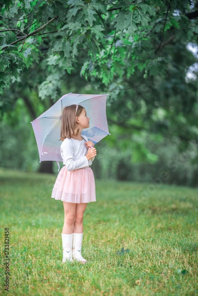 Fototapeta Little girl standing sideways under an umbrella and observing the wet landscape around her. Outdoor mindfulness and early interest in the changing rhythms of nature.