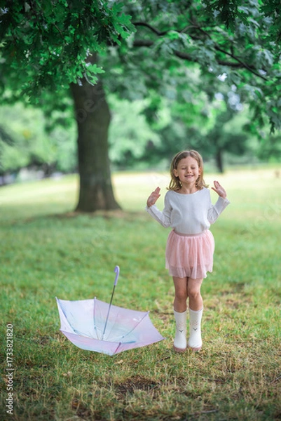 Fototapeta Little girl jumping in the air next to a closed umbrella lying on the ground. A burst of energy and spontaneous happiness on a rainy day.